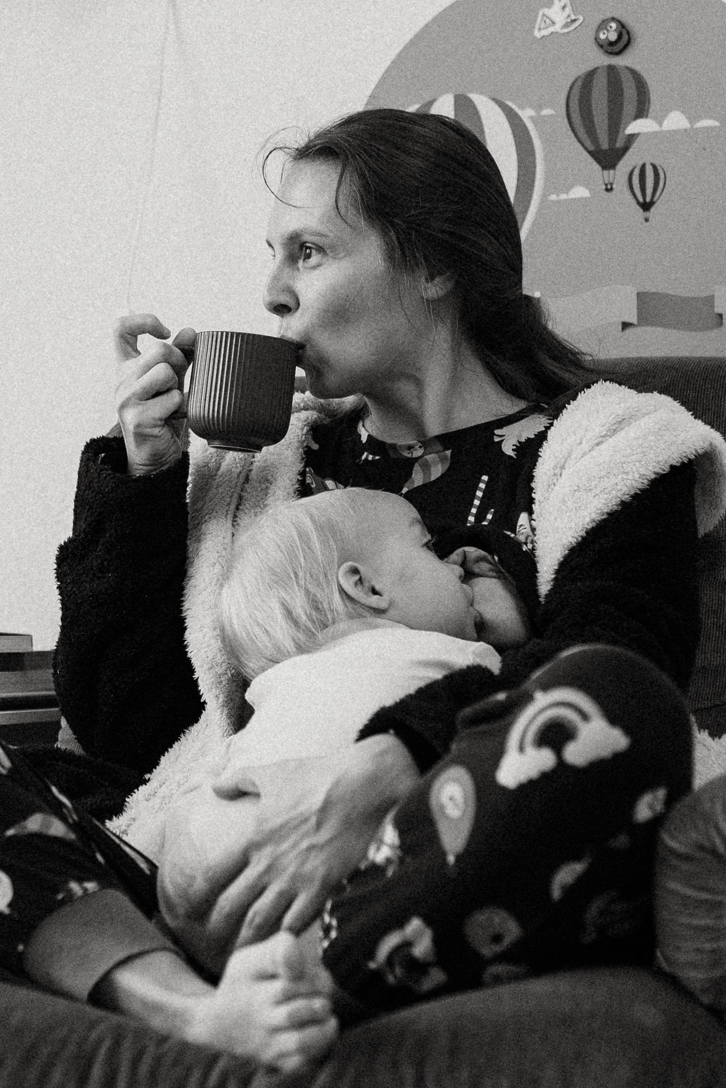 Mutter und stillendes Kind; die Mutter trinkt ihren Kaffee, während das Kind still